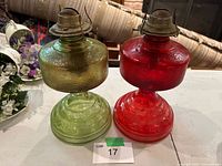 Front view of both red and green glass oil lamp bases showing colour, texture and metal burners