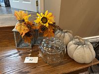 Group view of two cement pumpkins, clear glass pumpkin jar, two metal lanterns with fall foliage accents