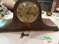 Front view of wooden tambour mantel clock showing brass dial, Arabic numerals, and winding key
