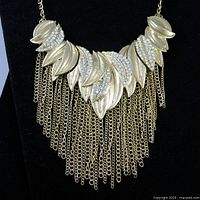 Front view of gold tone leaf motif crystal bib necklace with fringe