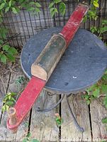 Full view of corn planter laid on table showing red wooden shaft and green metal seed hopper