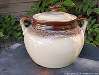 Front view of stoneware bean crock showing beige body, brown rim, lid, and side handles