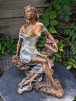 Full view of seated woman sculpture on rock base, bronze and silver finish