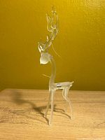 Full view of frosted glass reindeer ornament standing on wood surface