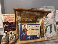 Overall view showing basket, Modern Home Sewing book, Compleat Family Book, toddler shoes, embroidery hoop