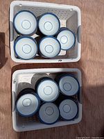 Two baskets containing approximately sixteen small white glass soup bowls with blue rim design