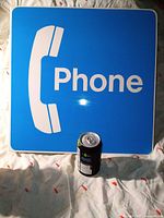 Front view of blue plastic phone sign with soda can for scale