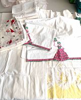 Stack of assorted pillowcases showing crochet lady pair, Santa print, plain whites with lace, overall view