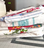 Stack of assorted folded vintage tablecloths showing different patterns and colours