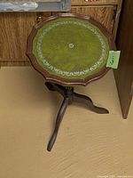 Full view of table showing green leather top, pie crust edge and tripod legs