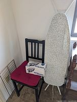 Corner view showing chair with boxed iron, ironing board, and wire rack