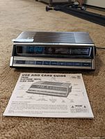 Full view of GE 7-4662 clock radio displaying 12:00 with manual in foreground