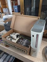 Console, two controllers and Alan Wake case inside cardboard box