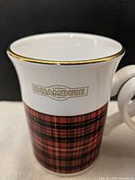 Close-up of mug front showing DRAMBUIE logo, tartan design, gold rim