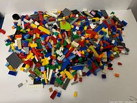 Large pile of assorted LEGO pieces spread out on white surface