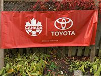 Full view English side showing Canada Soccer and Toyota logos, grommets along edge, plants for scale