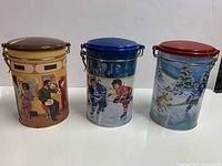 Front view of three Tim Hortons canisters showing artwork and lid colours