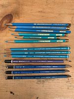 Group of turquoise Verithin pencils and blue Staedtler Lumochrom, Omnichrom and Non-Print pencils laid out on wood surface
