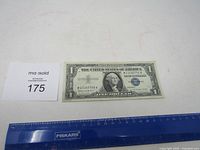 Full view of 1957B $1 silver certificate next to measuring scale and lot card
