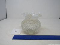 Front view of opalescent hobnail glass vase with ruffled rim next to ruler for scale