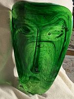 Front view of emerald green glass mask sculpture showing facial relief and seed bubbles