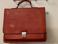 Front view of red leather Bruscoli Firenze briefcase showing flap, lock, and embossed monogram