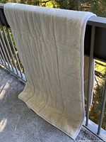Full view of quilted wool mattress pad hanging over railing
