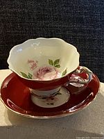 Teacup on saucer showing exterior red glaze, handle, gold trim