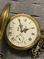 Open hunter-case pocket watch showing dial with Roman numerals and floral design