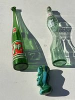 Green stretched 7-Up bottle, clear stretched Diet Coke bottle and glass head on white background