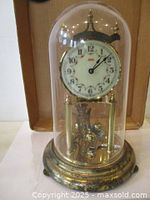 Front view of Kundo anniversary clock under glass dome on brass base
