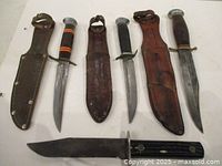 Seven items laid out: 4 Bowie knives, 3 leather sheaths
