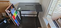 Front view of black adjustable drafting desk with side platform, canvases beside not included