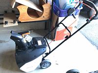 Side view of snow thrower showing handle, wheels, and housing