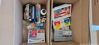 Overhead view of both cardboard boxes showing assorted art supplies and storage containers