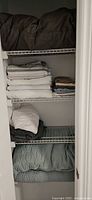 Closet shelves with dark grey comforter, stacks of fitted and flat sheets, pillowcases