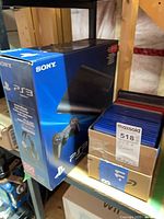 PS3 retail box beside cardboard box filled with blue PS3 disc cases