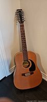 Full front view of Simon & Patrick 12-string acoustic guitar standing against wall