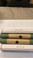 Two rolled olive green desk pads on white surface with Aothia boxes