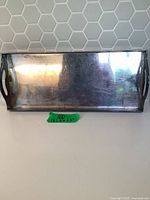 Front view of rectangular silver-tone metal tray showing handles and reflective surface