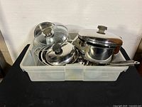 Assorted stainless steel pots and lids in plastic bin