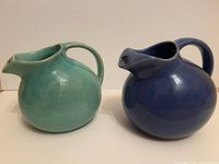 two spherical pottery pitchers, turquoise and blue, side by side