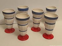 Six ceramic pedestal parfait cups front view showing red bases and blue stripes