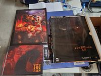 Three items laid out: God of War II guide, GoW III art book, Kratos poster
