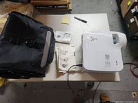 NEC projector, power cord, carrying bag, manuals on table