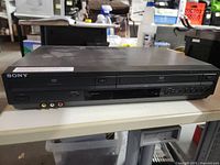 Front view showing Sony branding, DVD tray, VHS slot, front AV inputs and control buttons.