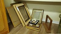 Stack of assorted gold-tone and smaller frames leaning against wall