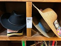 Shelf view showing black cowboy hat, stack of baseball caps, straw sun hat