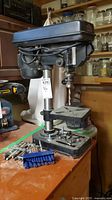 Side view of Jobmate benchtop drill press on bench with drill bits at base
