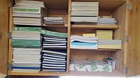 Cabinet shelves filled with stacked notebooks, notepads, copy paper, and sticky note pads